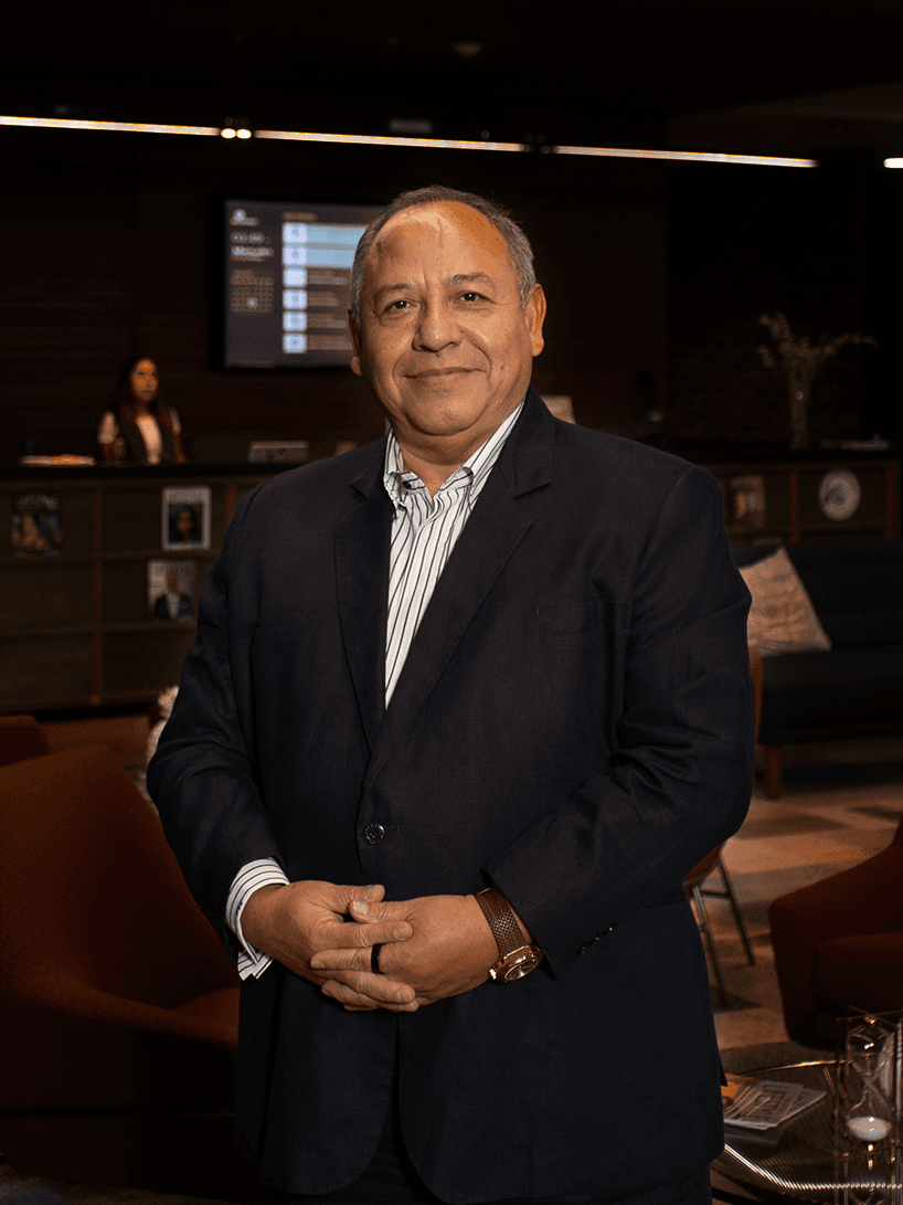 Smiling man in a navy blazer and striped shirt stands in a modern lounge area.
